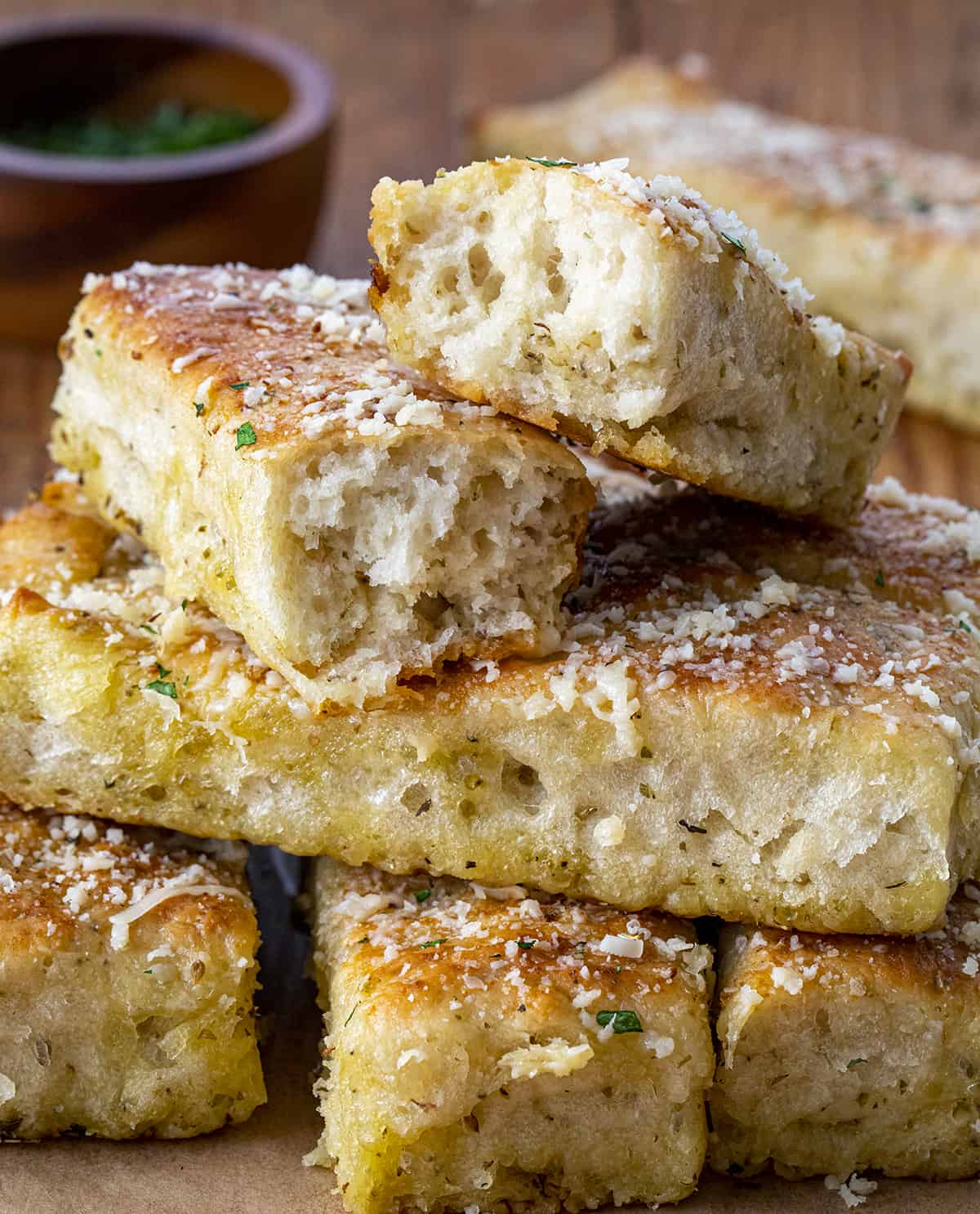 Stacks of Focaccia Breadsticks on a Cutting Board with Pieces Ripped in Half Showing Inside Texture.