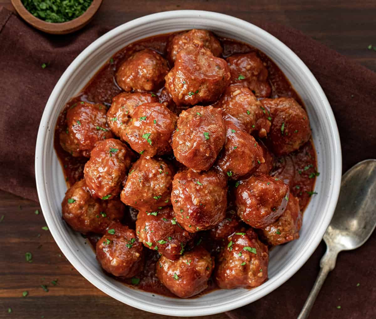 Bowl of Slow Cooker Cranberry Meatballs from Overhead with a Spoon Next to Bowl on Cutting Board.