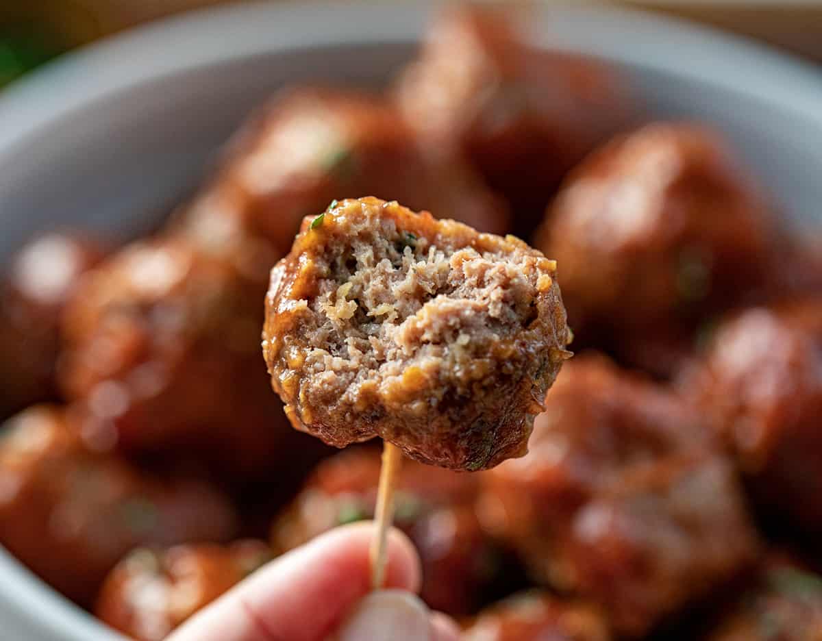 Hand Holding a Toothpick with a Bit Into Cranberry Meatball.