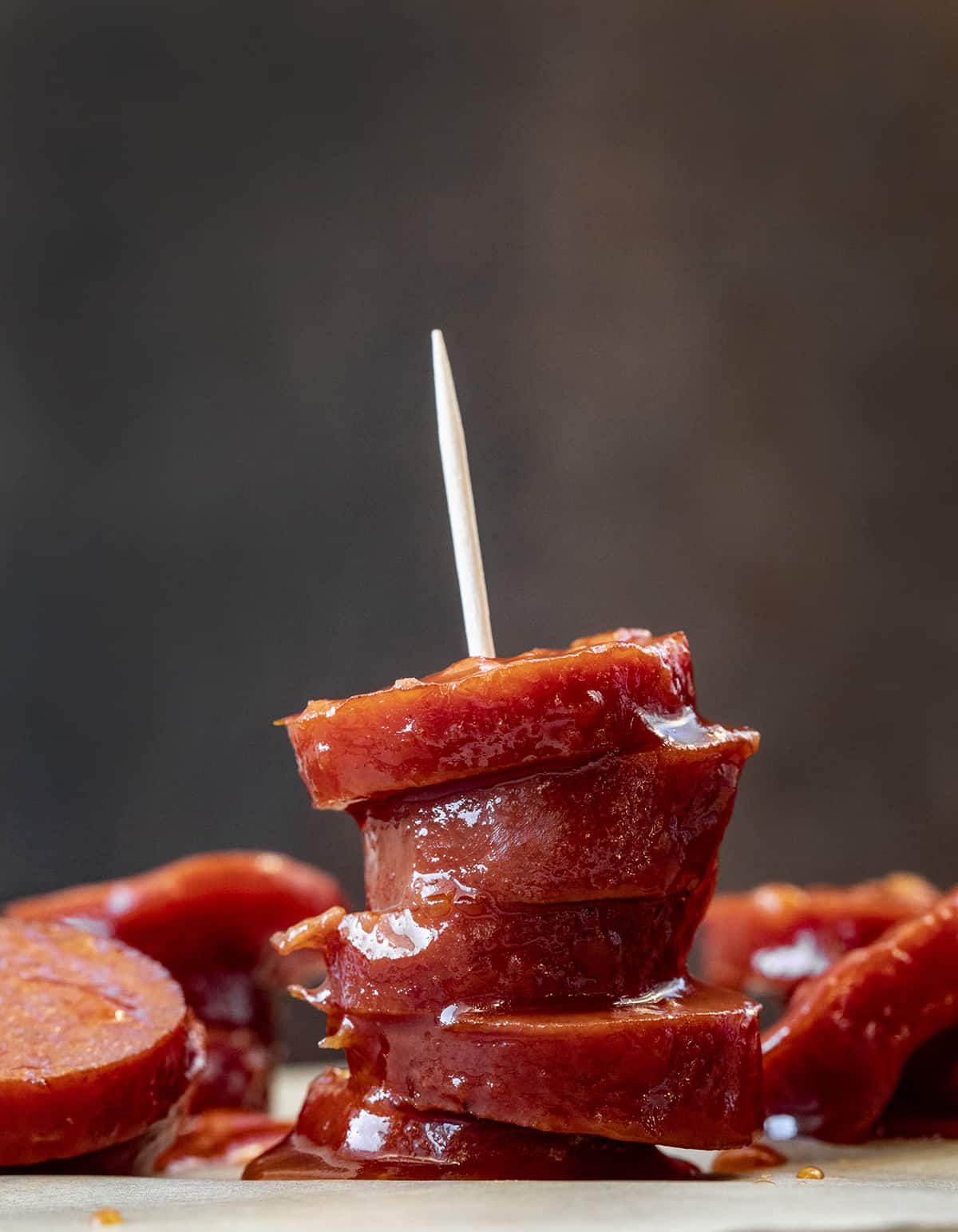 Pieces of Slow Cooker Bourbon Glazed Kielbasa Stacked on a Toothpick on a Cutting Board.