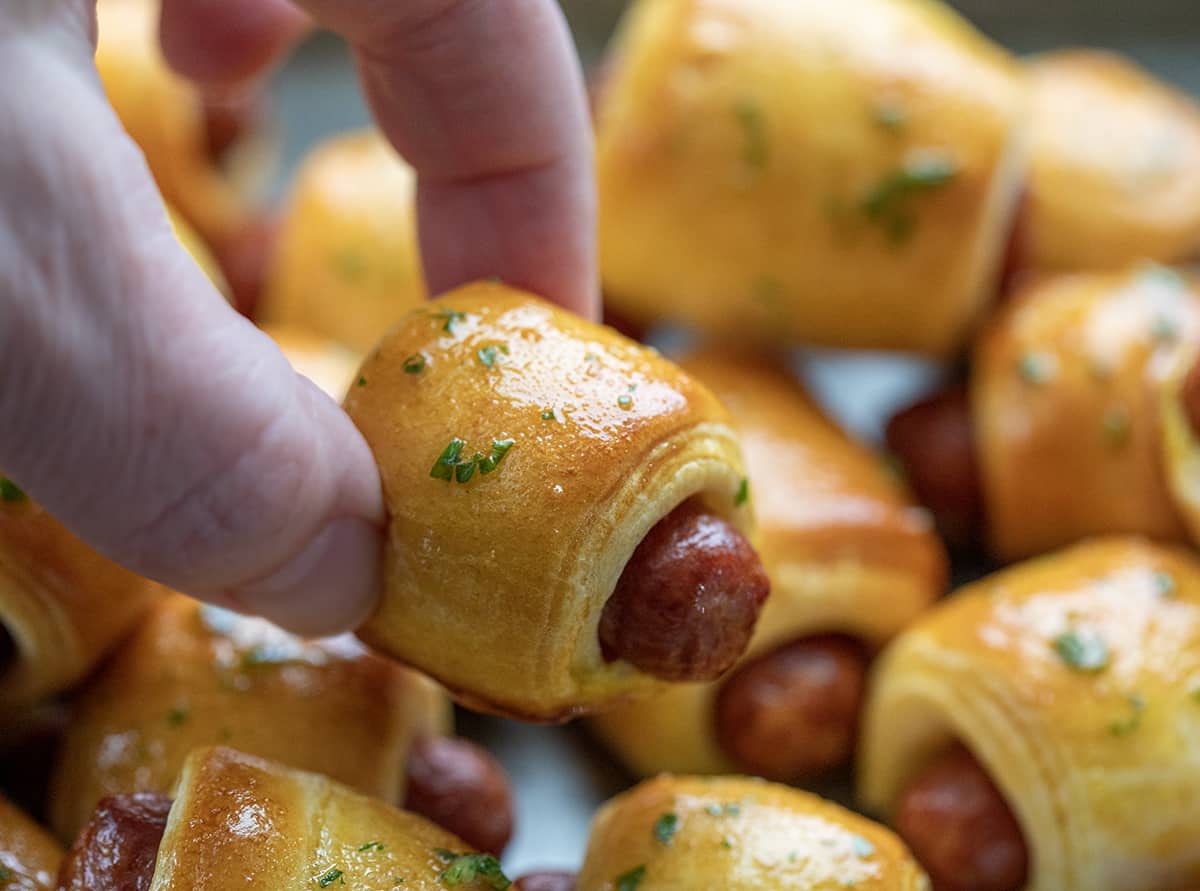 Hand holding one pigs in a blanket appetizer.