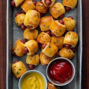 Pigs in a blanket in a pan with ketchup and mustard from overhead.