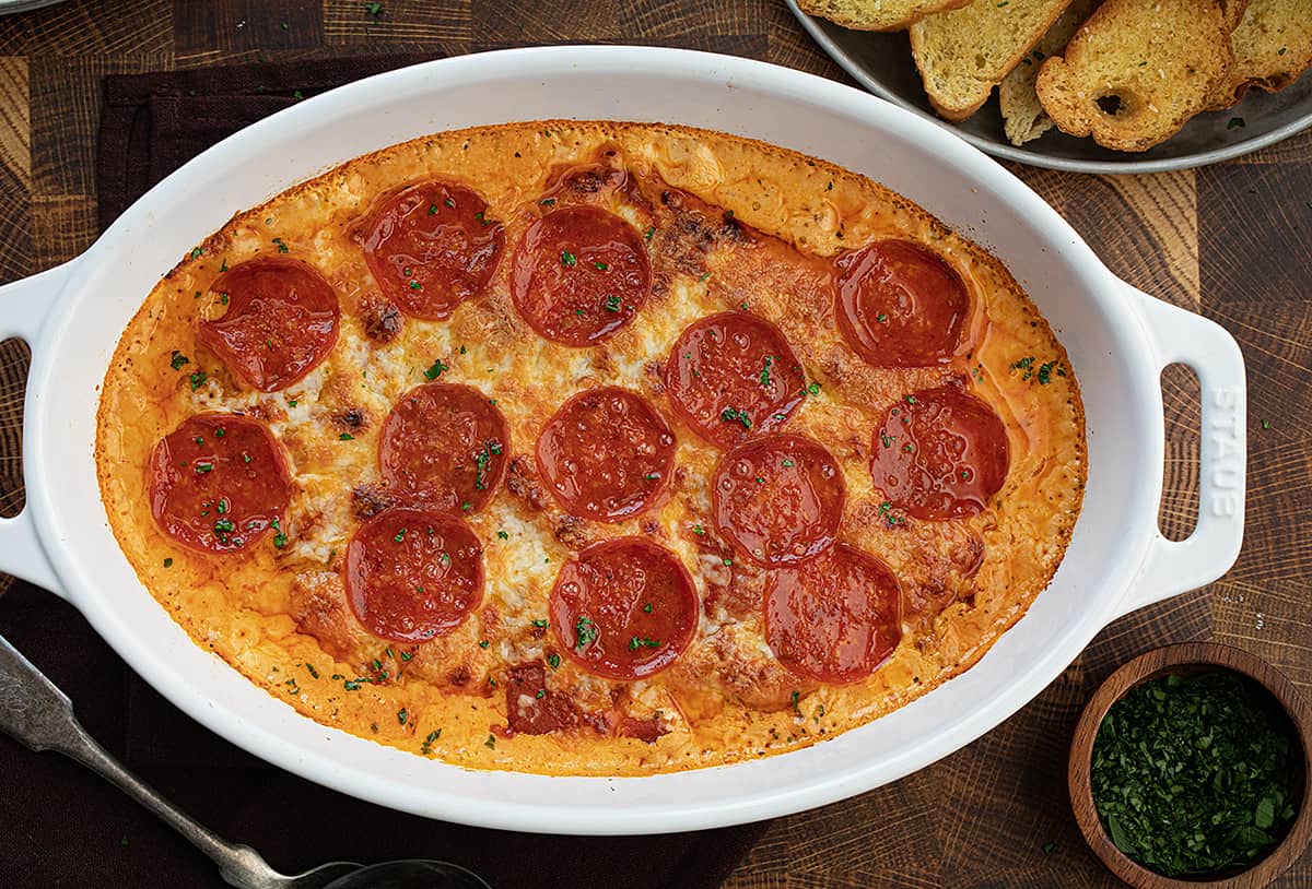 Pepperoni Pizza Dip in hot skillet on a butcher block with crostini. 