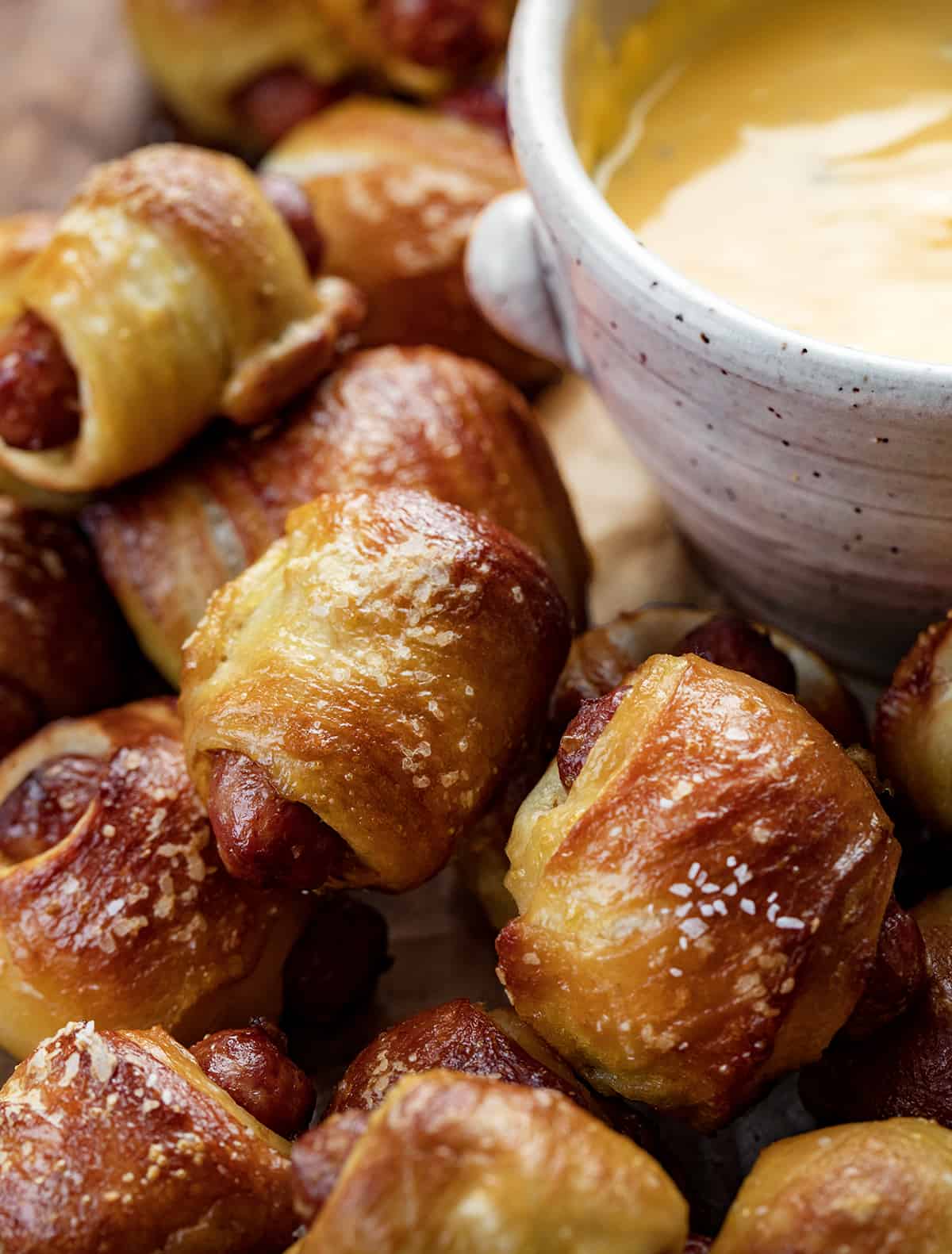 Close up of Pretzel Pigs in a Blanket Next to a Bowl with Cheese.