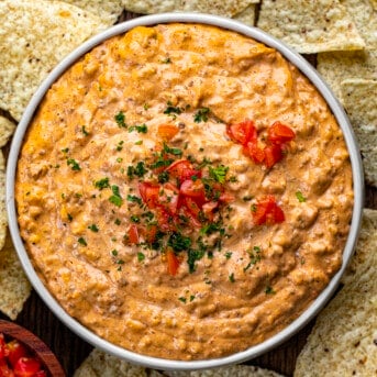 Bowl of Slow Cooker Taco Dip on a Cutting Board Surrounded by Tortilla Chips.