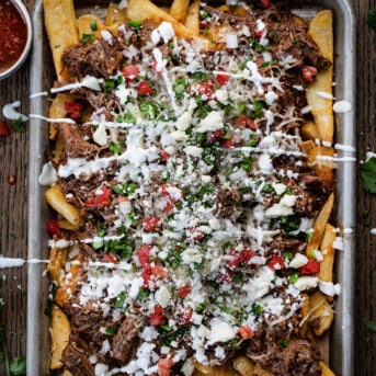 Sheet Pan of Loaded Shredded Beef {Birria} French Fries Covered in Sour Cream, Tomatoes, and Cilantro.