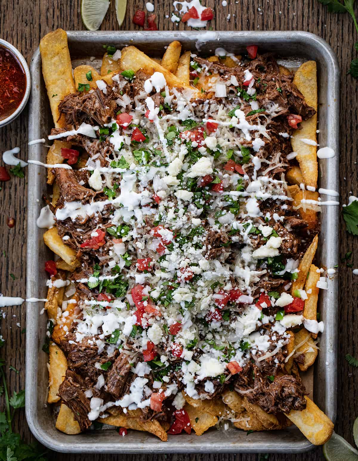 Sheet Pan of Loaded Shredded Beef {Birria} French Fries Covered in Sour Cream, Tomatoes, and Cilantro.