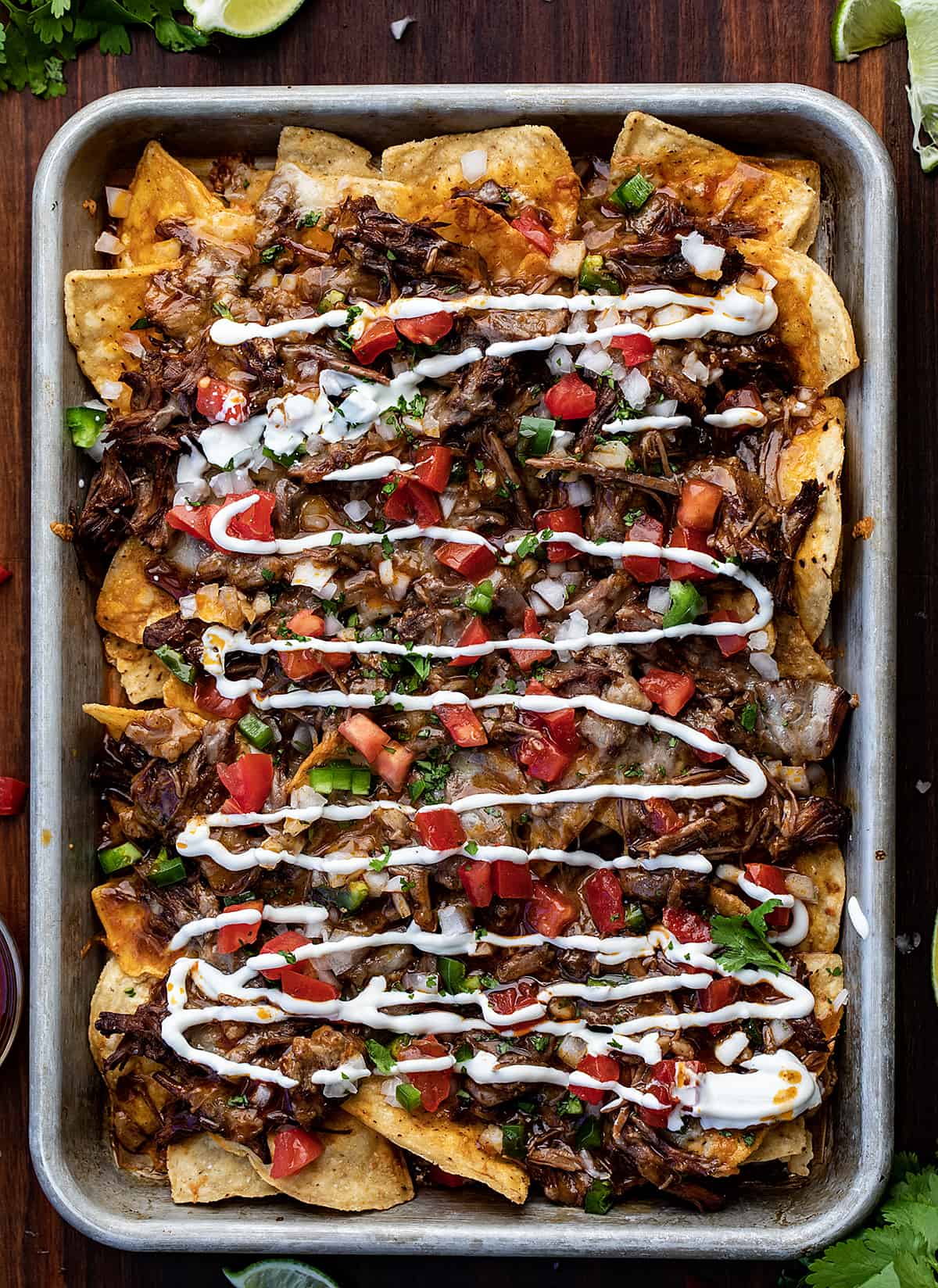 Pan of Birria Nachos on a cutting Board Surrounded by Limes and Sauce. 