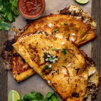 Birria Quesadilla - Shredded Beef Quesadillas on a Cutting Board with Cilantro and Birria Sauce.