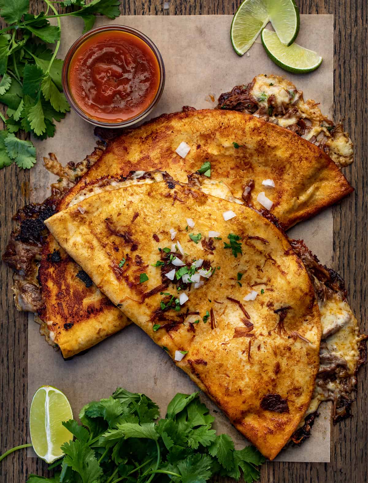 Birria Quesadilla - Shredded Beef Quesadillas on a Cutting Board with Cilantro and Birria Sauce.