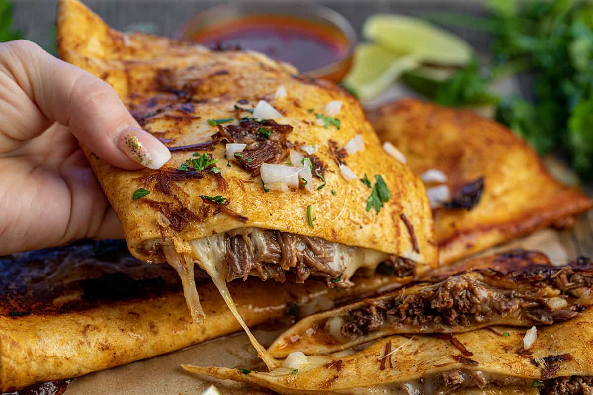 Hand Picking up a Cut in Half Birria Quesadilla.