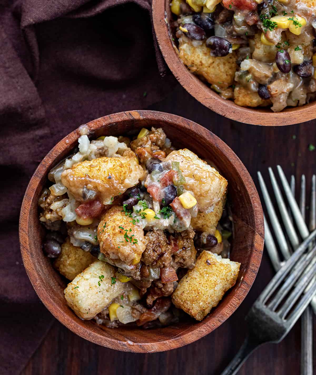 Bowls of Cowboy Tater Tot Casserole with Forks on a Cutting Board.