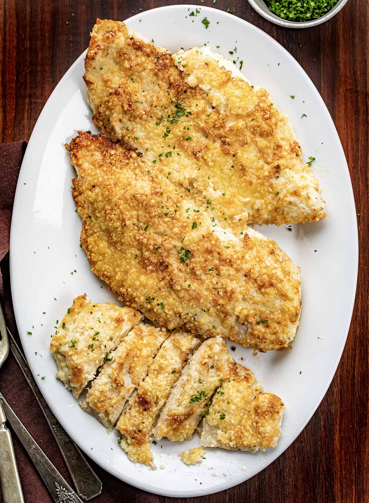 Platter of Mayonnaise Parmesan Chicken on a Cutting Board with Silverware.