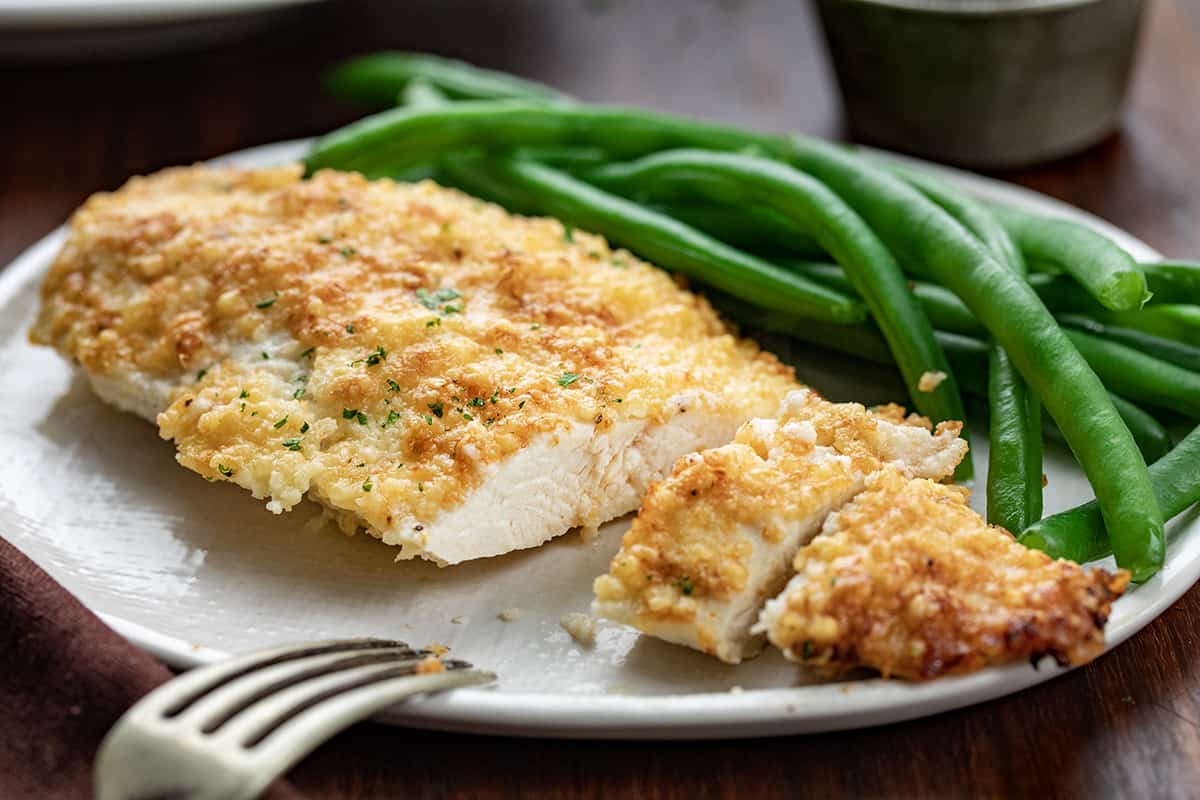Piece of Mayonnaise Parmesan Chicken on Plate with Green Beans and Chicken is Cut Into Showing Inside.
