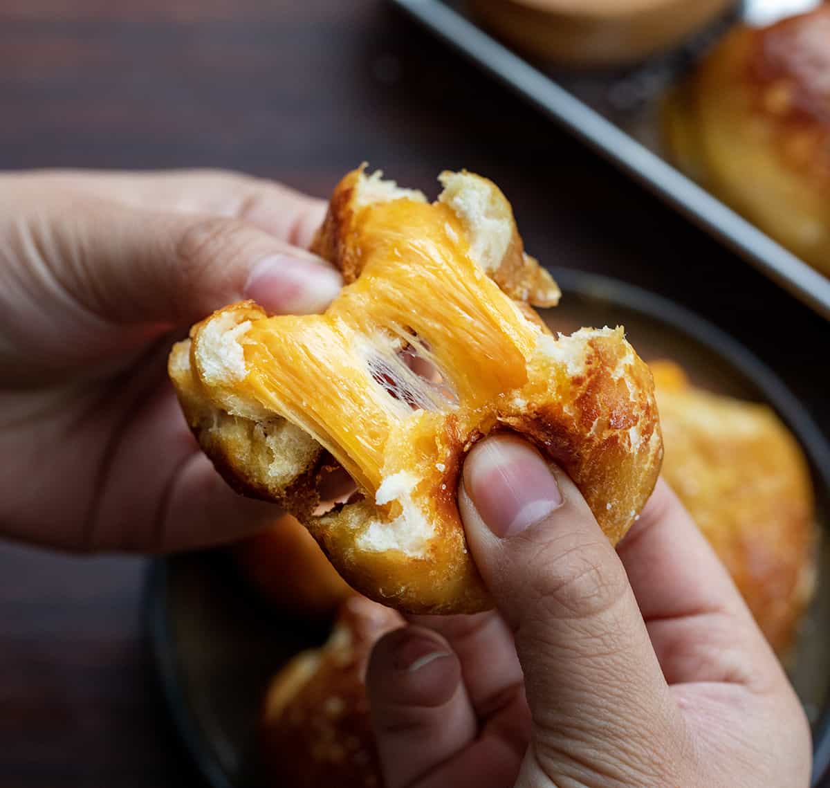 Hands Pulling Apart a Chessy Stuffed Pretzel Bomb Showing the Cheese Stretching Inside.