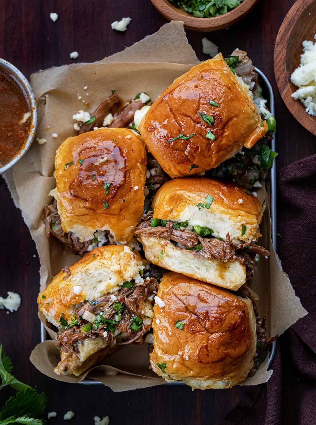Pan of Shredded Beef Sliders Next to the Sauce on a Cutting Board.