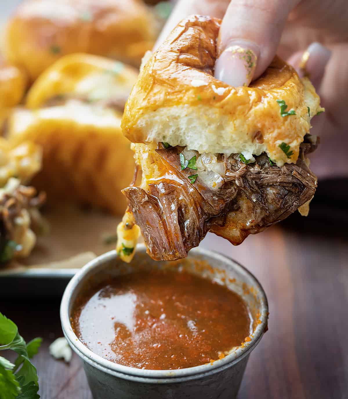 Hand Holding a Shredded Beef Slider and Dipping into Sauce.