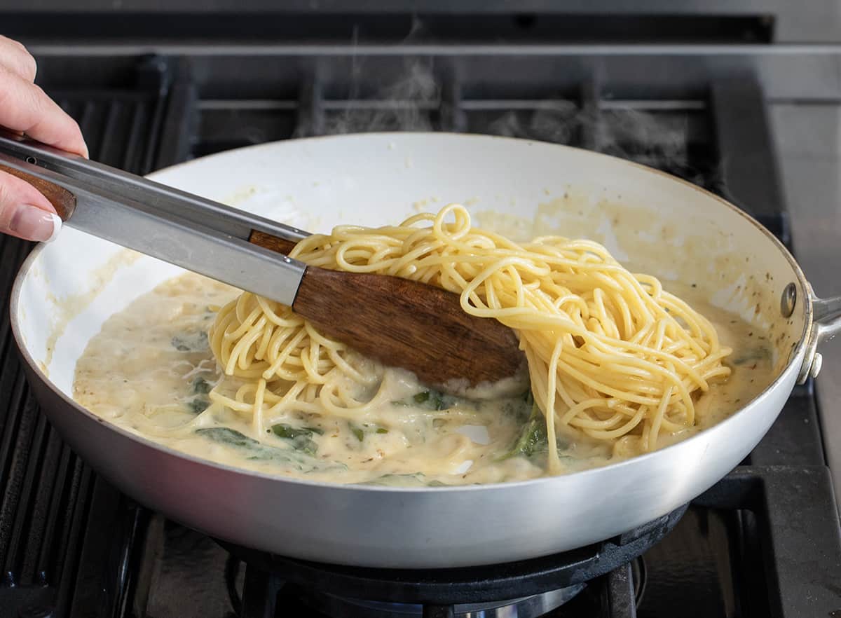 Tongs Stirring Pasta in to Asiago Cheese Sauce.