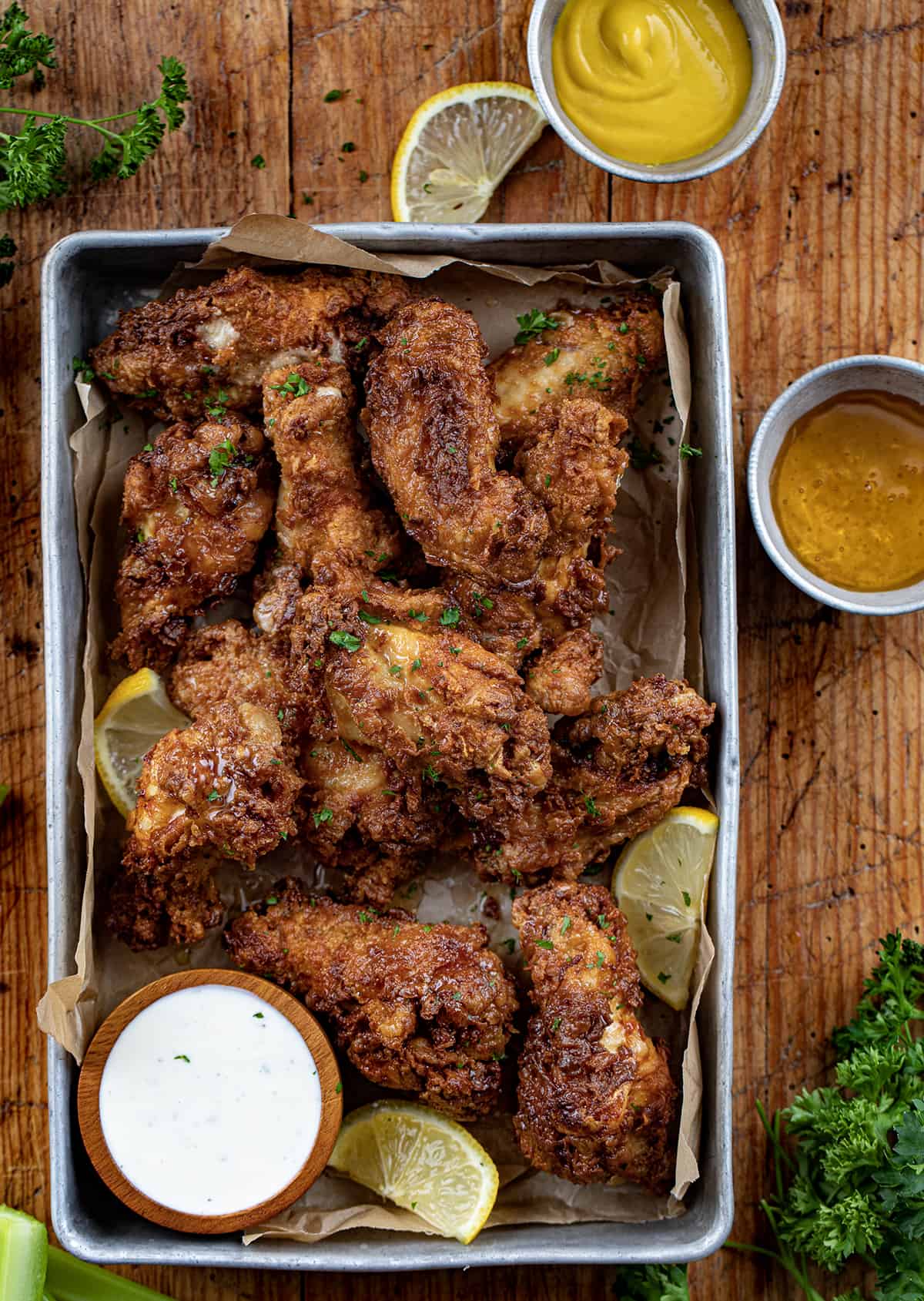 Pan of Buffalo Honey Mustard Chicken Wings with Homemade Ranch Dressing, Honey, Mustard, and Lemons on the Side.