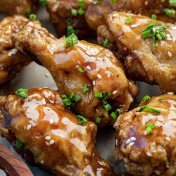 Close up of Teriyaki Chicken Wings Next to Sauce and Covered in Sesame Seeds.