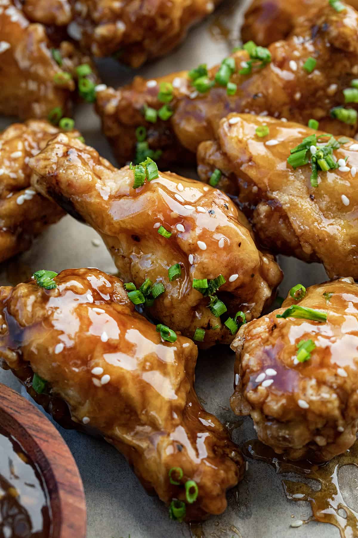 Close up of Teriyaki Chicken Wings Next to Sauce and Covered in Sesame Seeds.