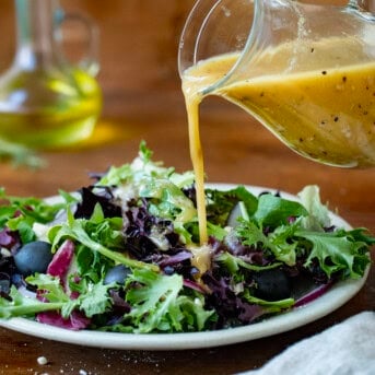 Pouring Homemade Greek Vinaigrette over salad.