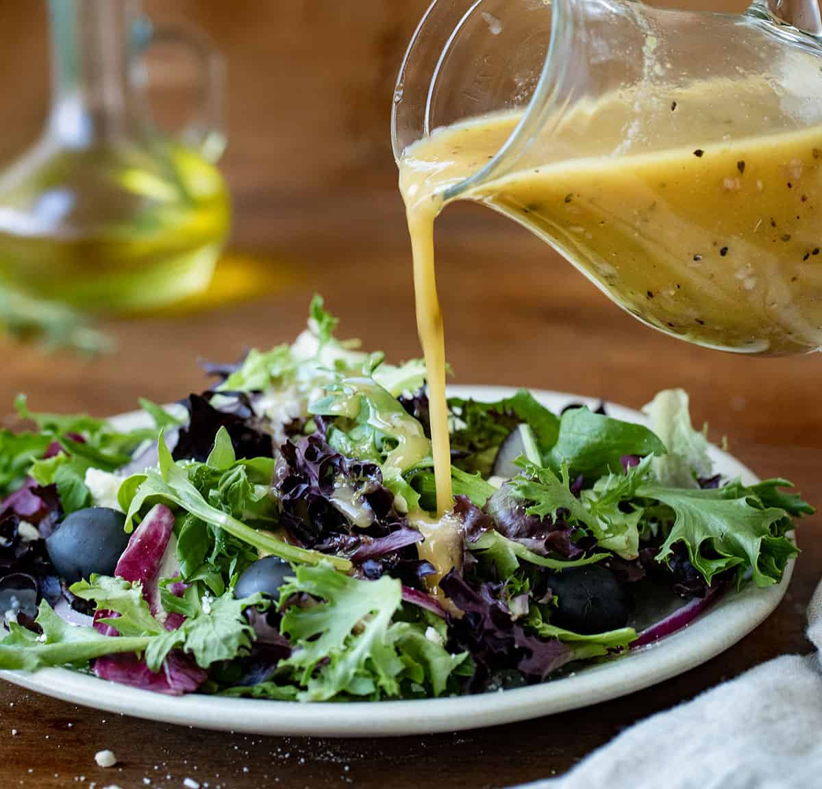 Pouring Homemade Greek Vinaigrette over salad.