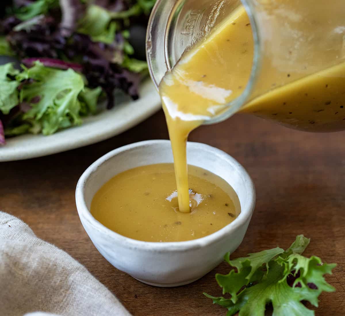 Pouring Homemade Greek Vinaigrette into a dish.