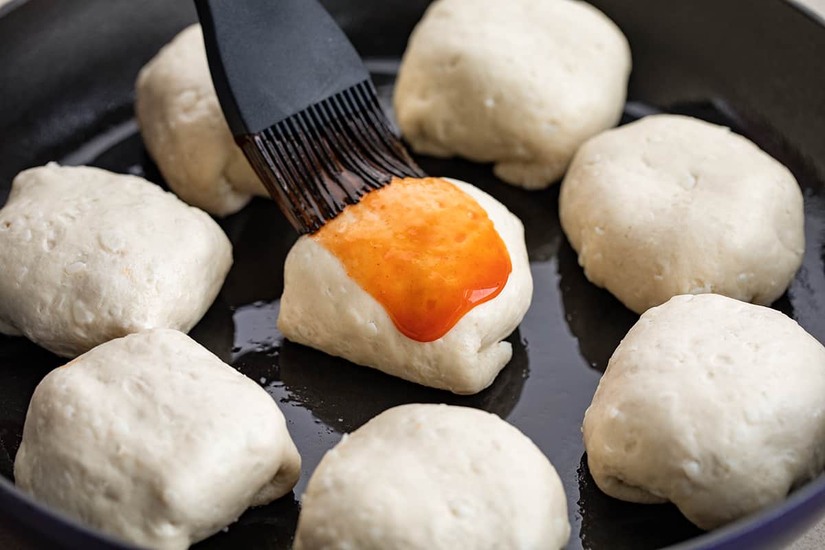 Brushing Buffalo Sauce Over Buffalo Chicken Loaded Biscuits in a Pan.