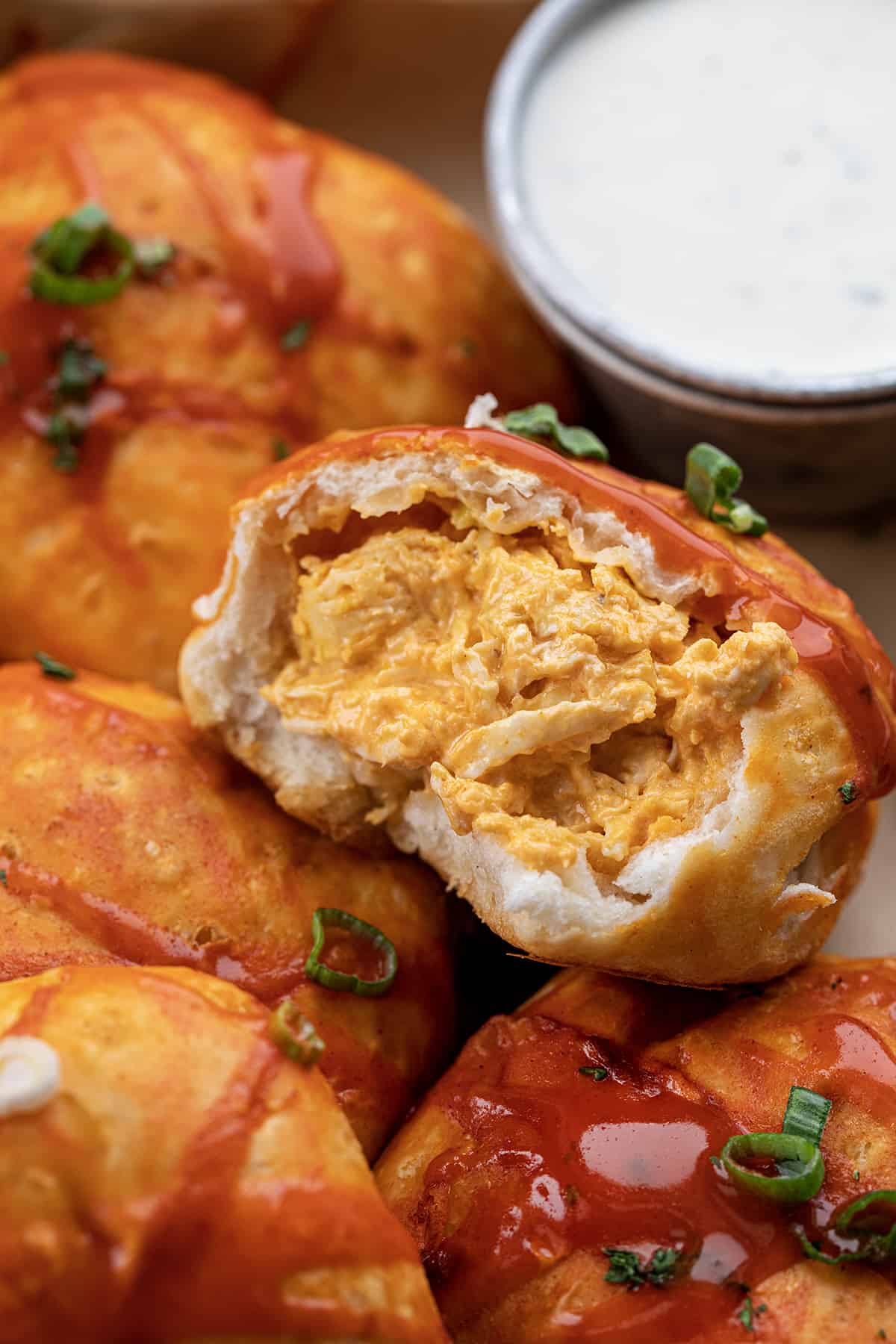 Buffalo Chicken Bombs in a Pan with Ranch Dressing and One Bomb Cut in Half Showing the Inside After Baking.