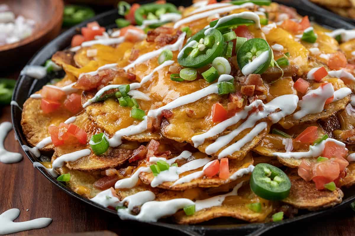 Close up of Skillet of Irish Nachos Covered in Toppings and Sour Cream.
