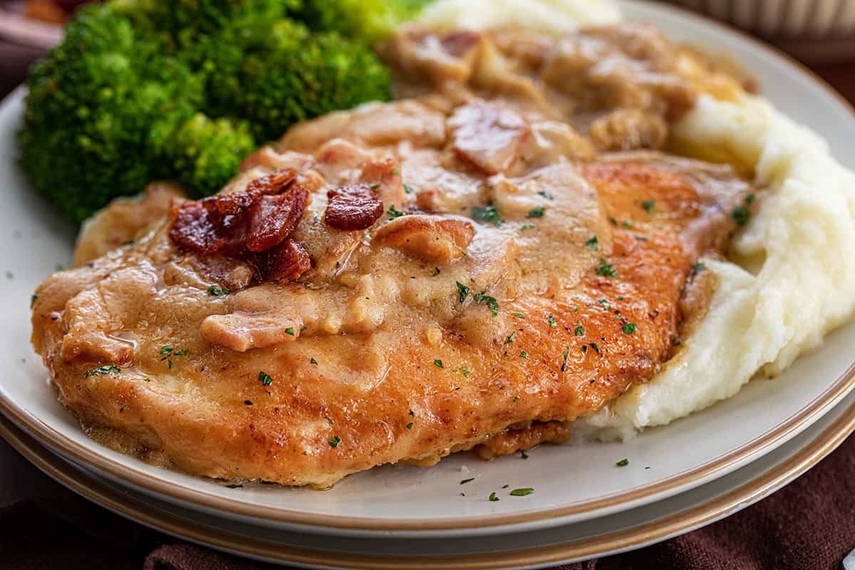 PIece of Smothered Chicken on a Plate with Mashed Potatoes and Broccoli.
