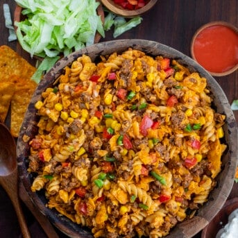 Bowl of Taco Pasta Salad from Overhead on a Dark Cutting Board with Lettuce and Dressing Next to It.