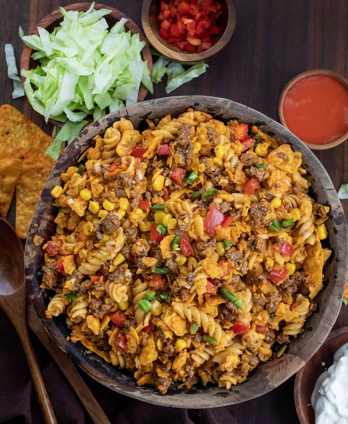 Bowl of Taco Pasta Salad from Overhead on a Dark Cutting Board with Lettuce and Dressing Next to It. 