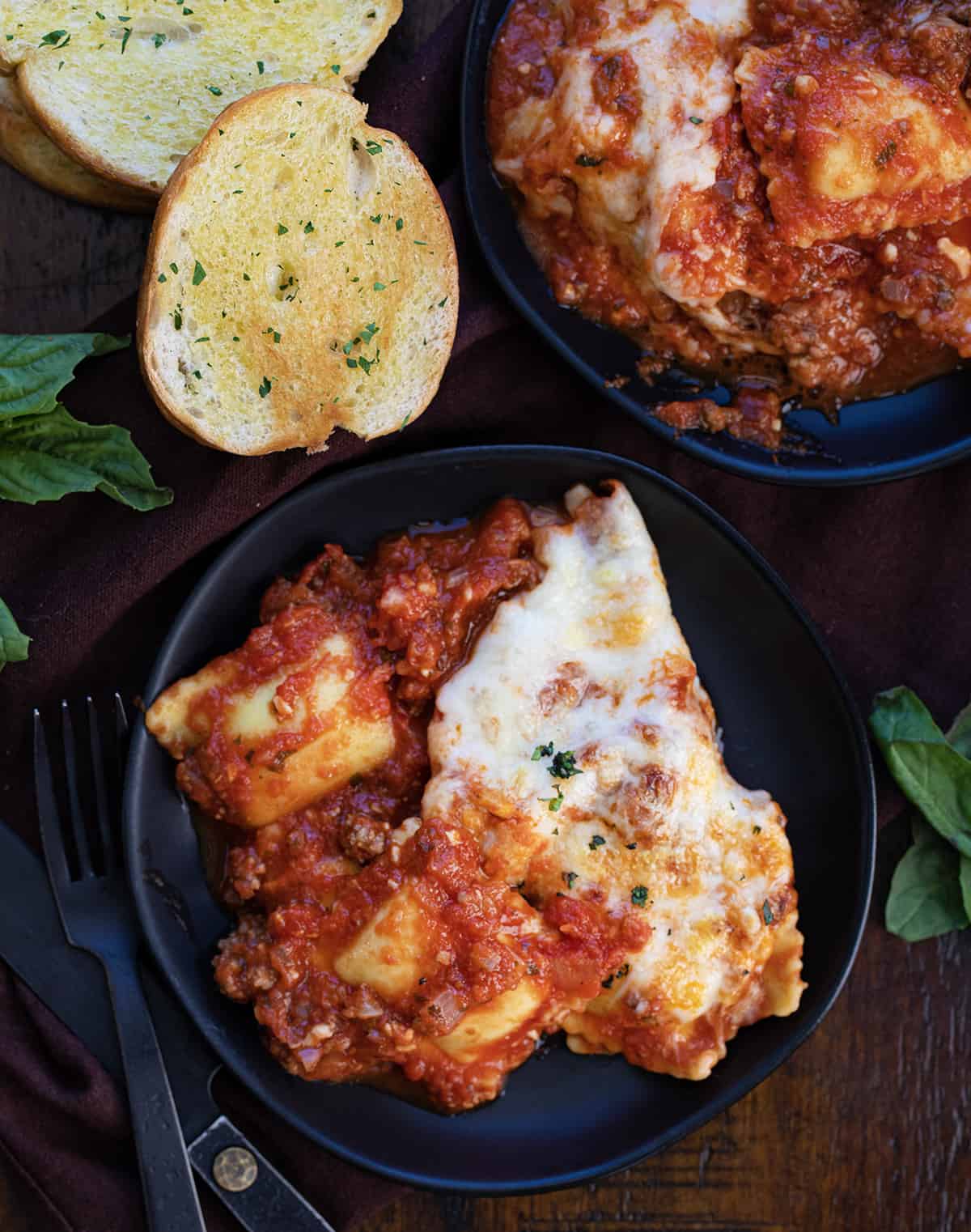 Two plates of Skillet Ravioli on a dark cutting Board.