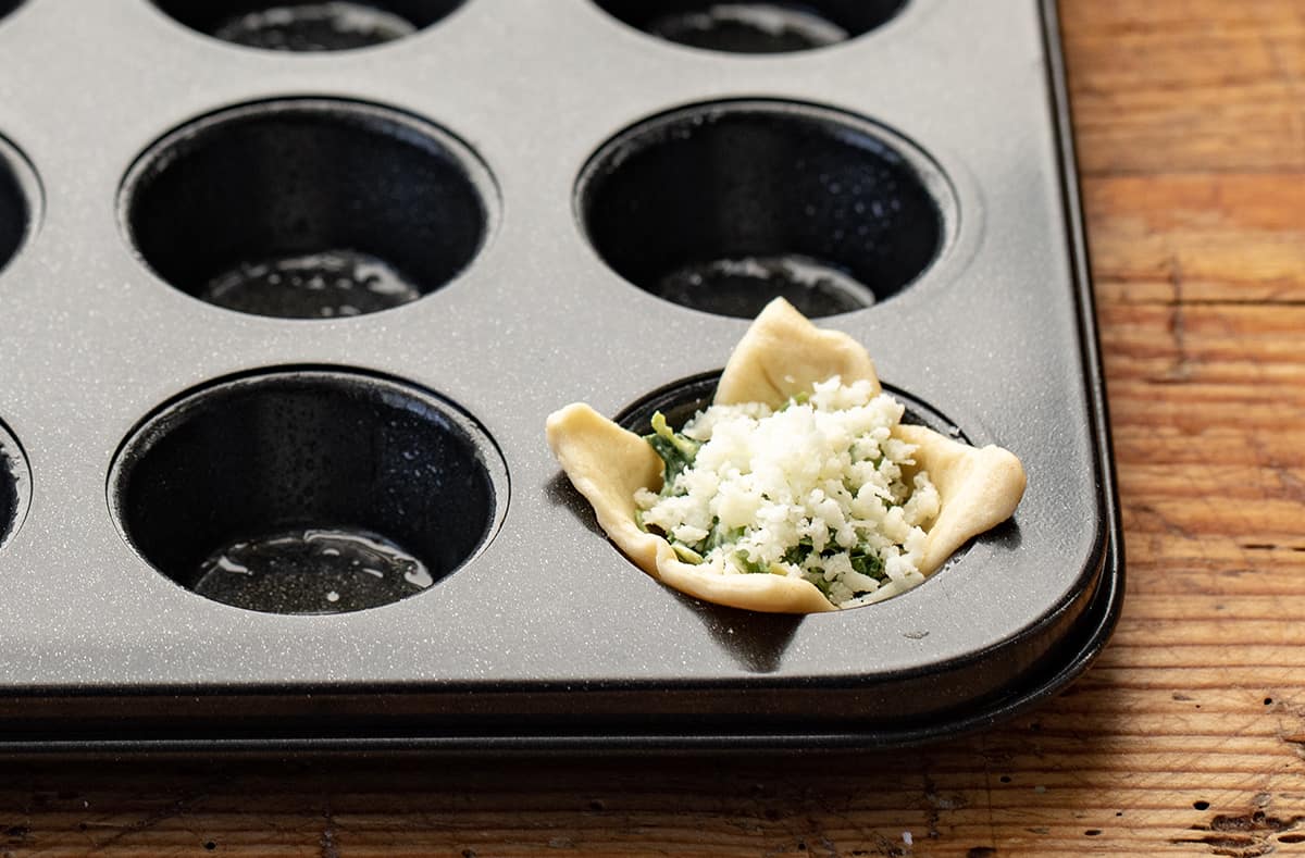 Adding Dough, Spinach Dip, and Cheese to Mini Muffin Pan to Make Spinach Dip Bites.