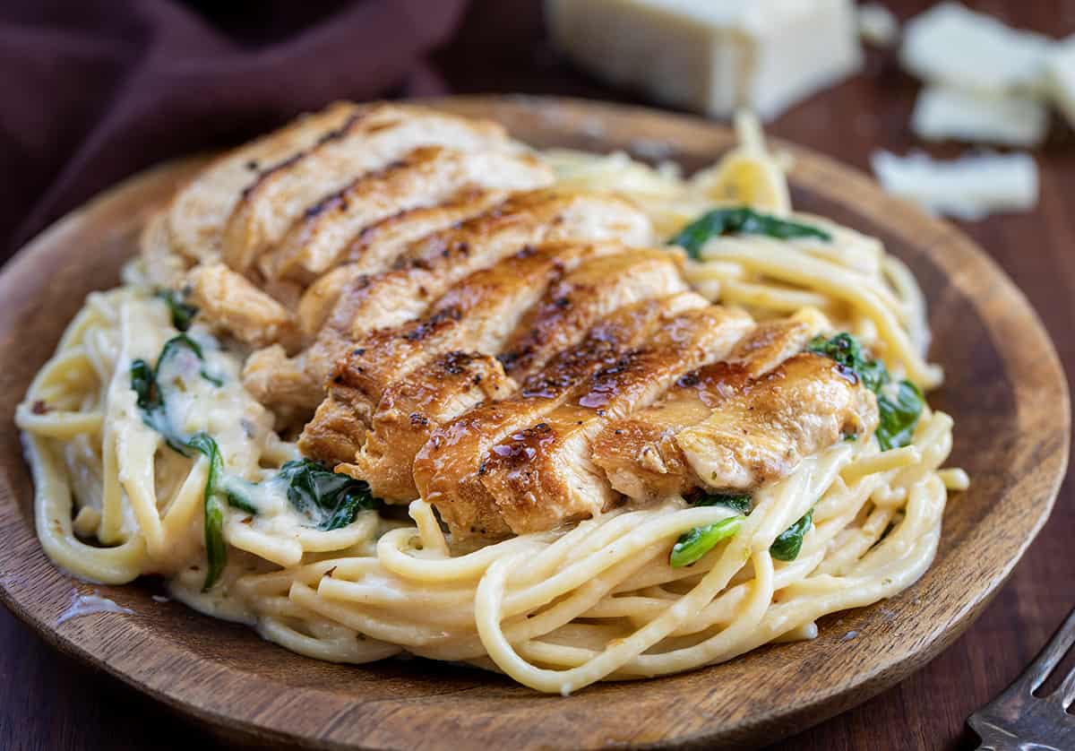 Plated Asiago Chicken Pasta on a Wooden Plate on a Dark Counter.