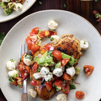 Plated Balsamic Chicken With Caprese Salsa on Light Plates on a Dark Cutting Board.