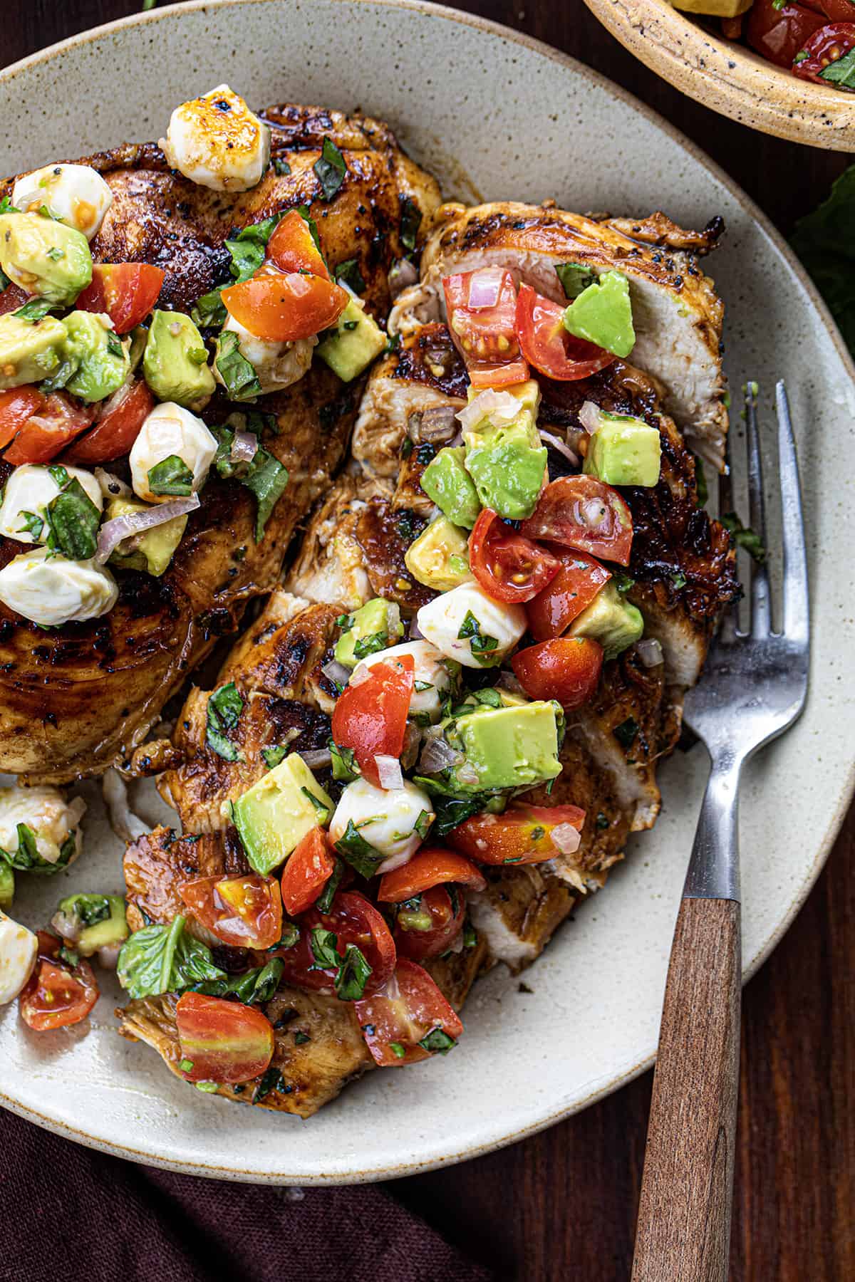 Plated Balsamic Chicken With Caprese Salsa on Light Plates on a Dark Cutting Board.