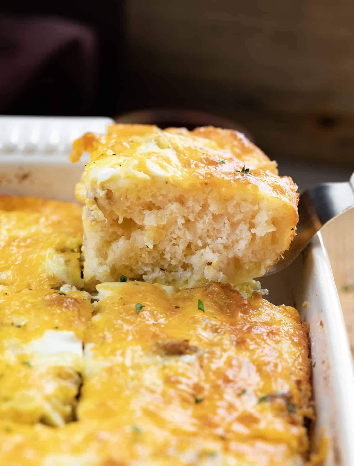 Spatula Picking up a Piece of Butter Biscuit Breakfast Bake from Hot Casserole Dish.