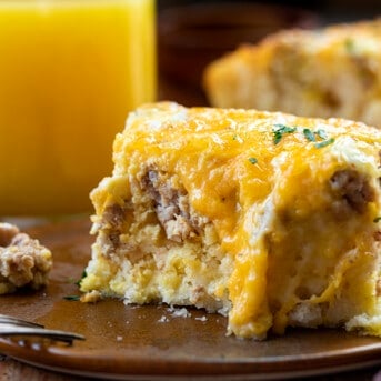Piece of Butter Biscuit Breakfast Bake on a Plate with a Bite Removed and Orange Juice in the Background.