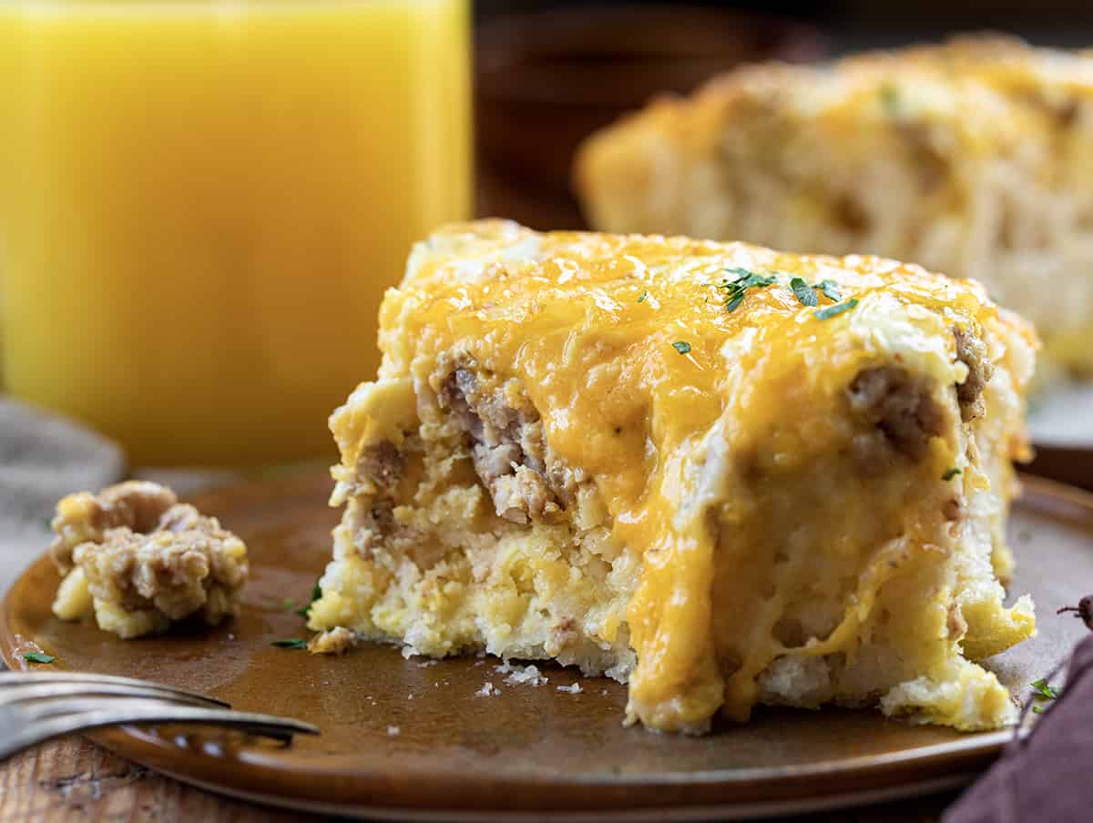 Piece of Butter Biscuit Breakfast Bake on a Plate with a Bite Removed and Orange Juice in the Background.