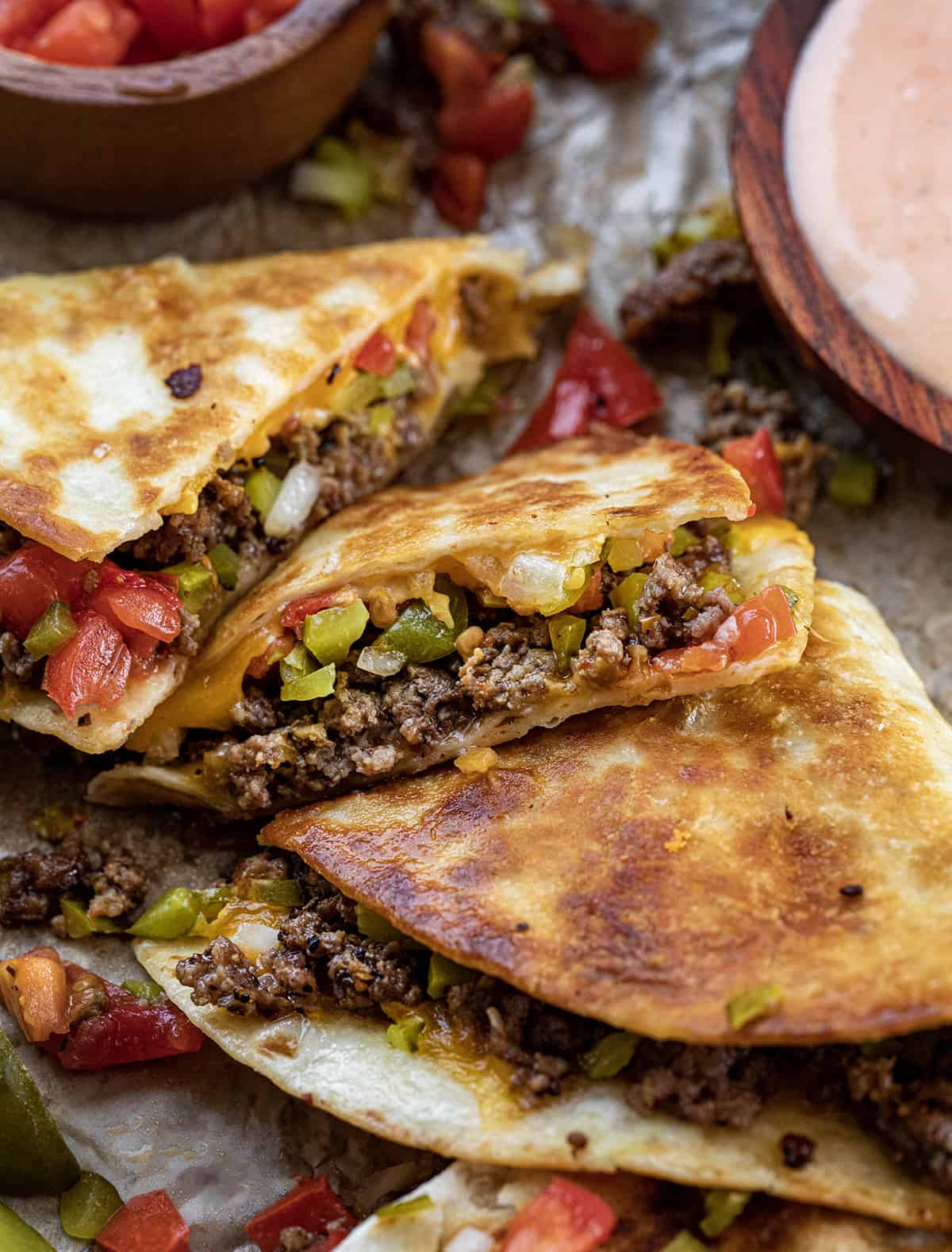 Whole and Cut Up Cheeseburger Quesadillas on a Piece of Parchment Next to Fry Sauce.