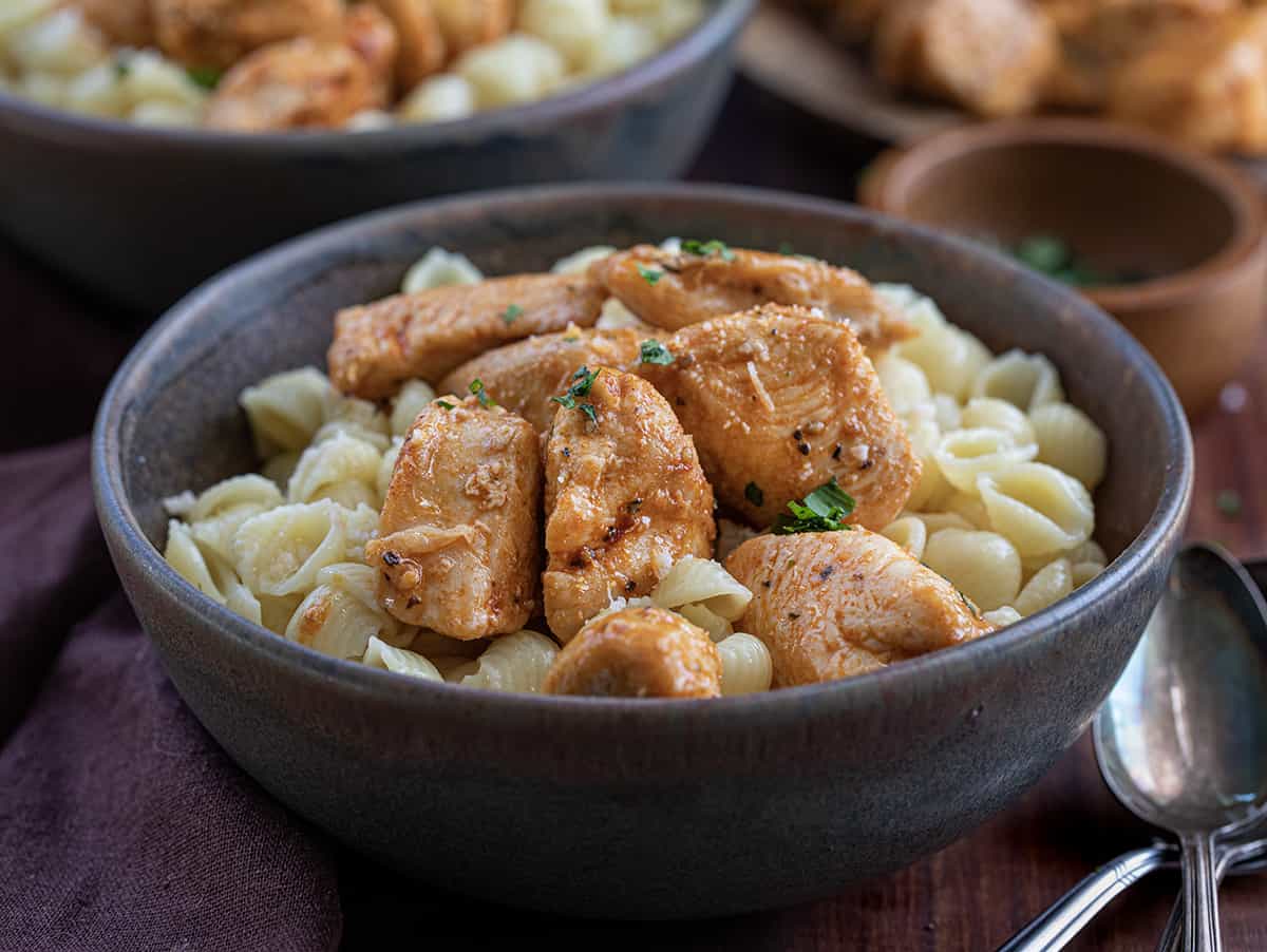 Bowls of Chicken and Buttered Noodles on a Cutting Board with Silverware Next to It.