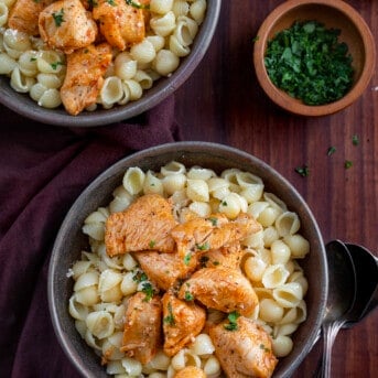 Two Black Bowls Filled with Chicken Bites and Buttered Noodles on a Cutting Board.