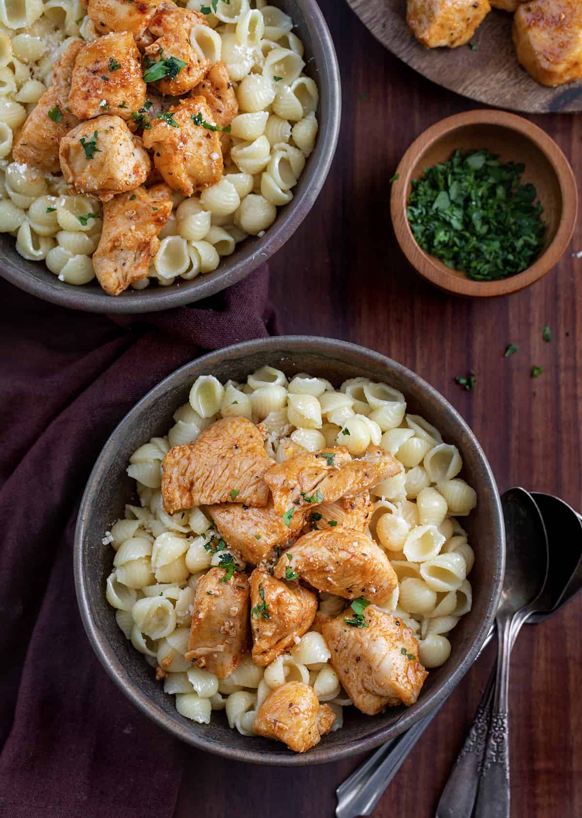 Two Black Bowls Filled with Chicken Bites and Buttered Noodles on a Cutting Board.
