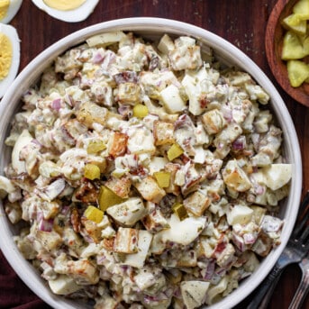 Big Bowl of Dill Pickle Roasted Potato Salad Next to Pickles and Cut up Eggs.