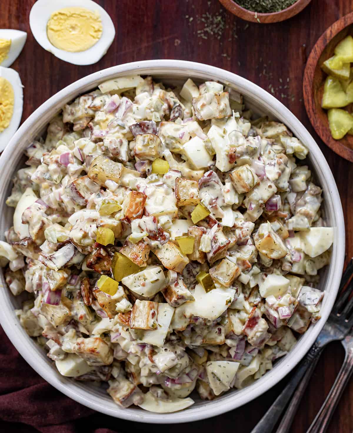 Big Bowl of Dill Pickle Roasted Potato Salad Next to Pickles and Cut up Eggs.