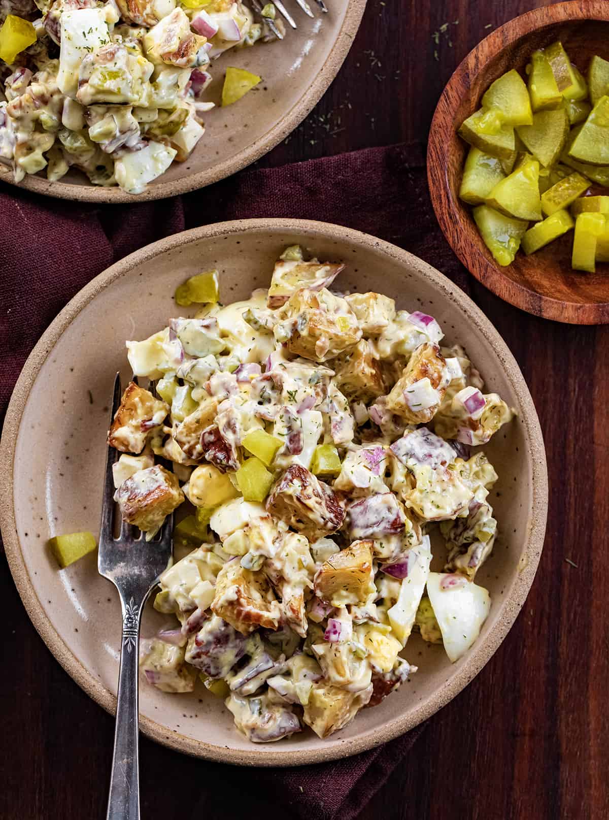 Plates with Dill Pickle Roasted Potato Salad on Them on a Dark Cutting Board and Pickles.