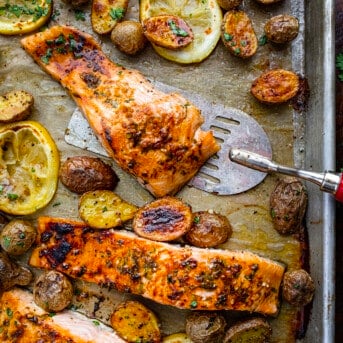 Picking up a Piece of Salmon from a Sheet Pan with Lemons and Potatoes.